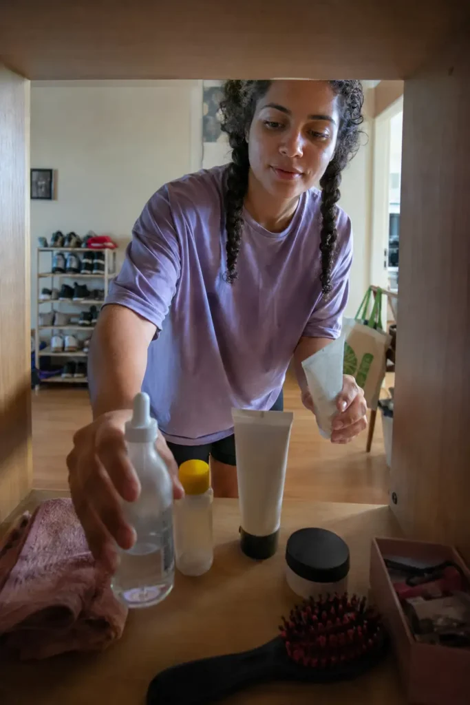 Mulher jovem organizando poucos produtos de skincare em uma pequena prateleira