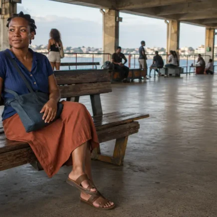 Mulher jovem sentada em terminal hidroviário brasileiro, tranquila e presente enquanto aguarda o embarque.